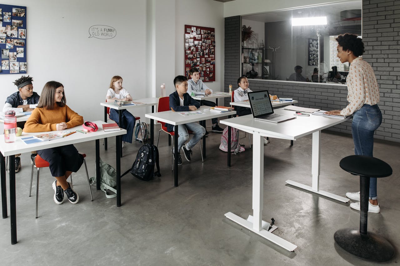 A diverse group of students attentively listens to a teacher in a modern classroom setting.