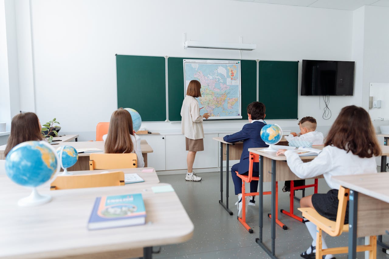 About Students engaged in a geography lesson, focusing on a wall map in a classroom with globes and study materials.